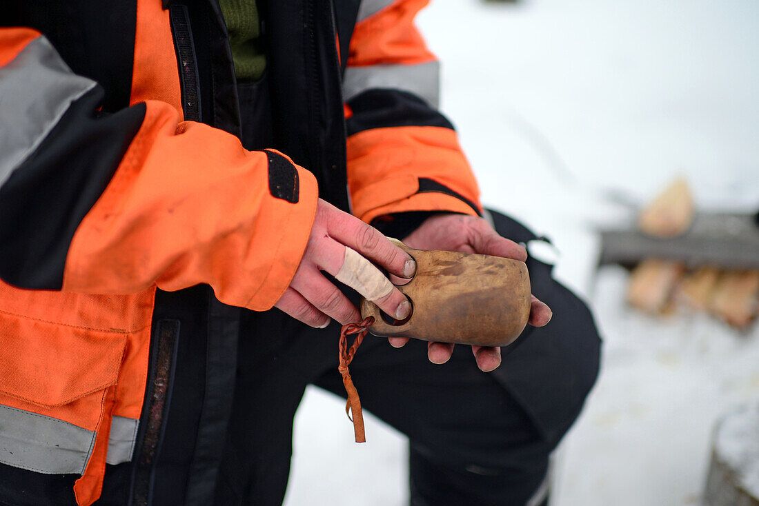 Antti hält eine Kuksa, einen traditionellen lappländischen Holzbecher aus Birkenwurzelholz, während einer Schneemobilfahrt über den Inari-See. Lappland, Finnland