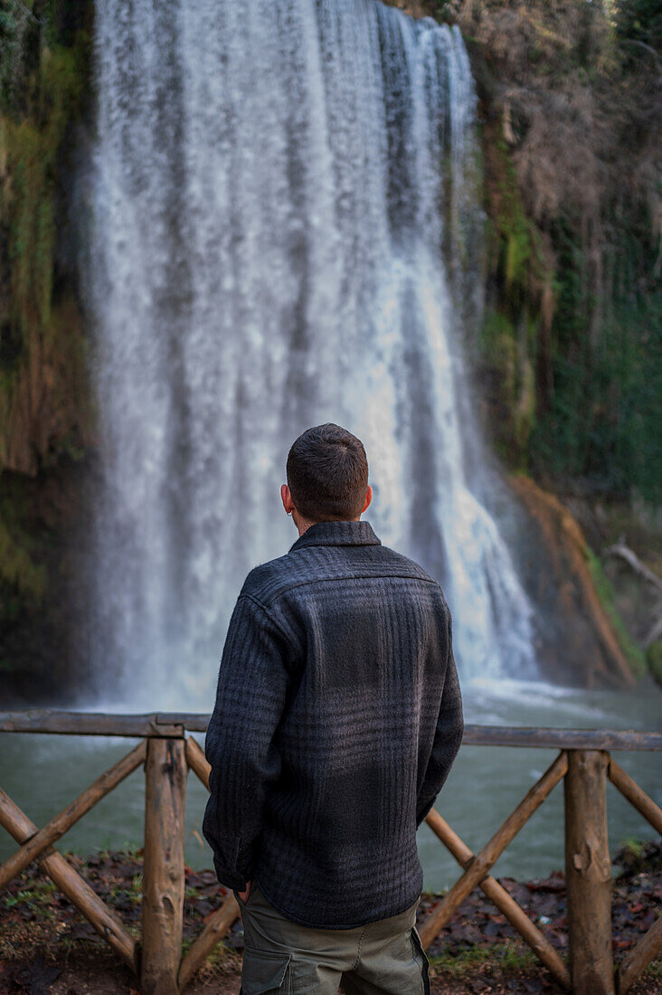 Junger Mann betrachtet einen Wasserfall im Naturpark Monasterio de Piedra, der sich um das Monasterio de Piedra (Steinkloster) in Nuevalos, Zaragoza, Spanien, befindet