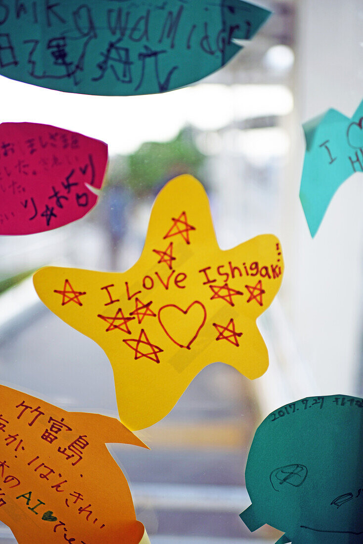 Von Kindern gebastelte Zettel in Fischform schmücken die Glasfenster im Hafen von Taketomi, Okinawa, Japan