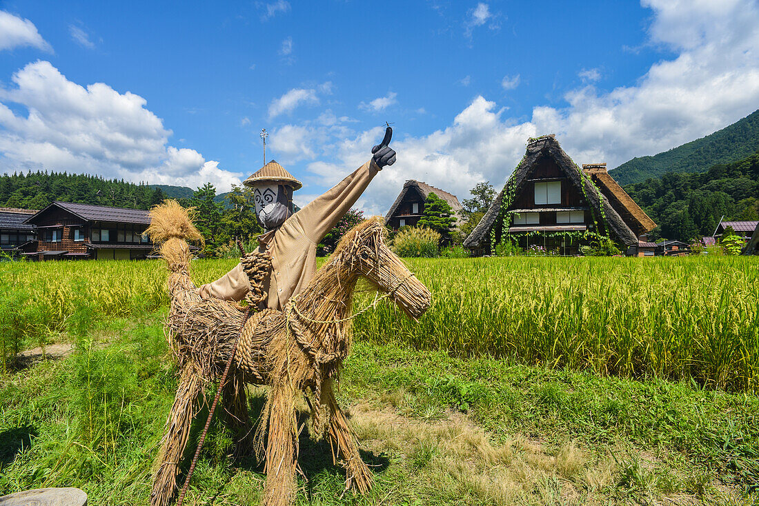 Vogelscheuchen vor traditionellen Gassho-Zukuri-Holzhäusern mit Strohdach im Dorf Shirakawa-go, Präfektur Gifu, Japan