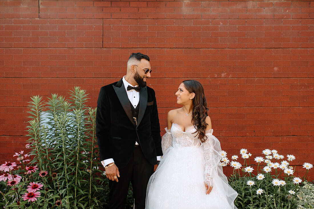 Smiling bride and groom against brick wall and flowers