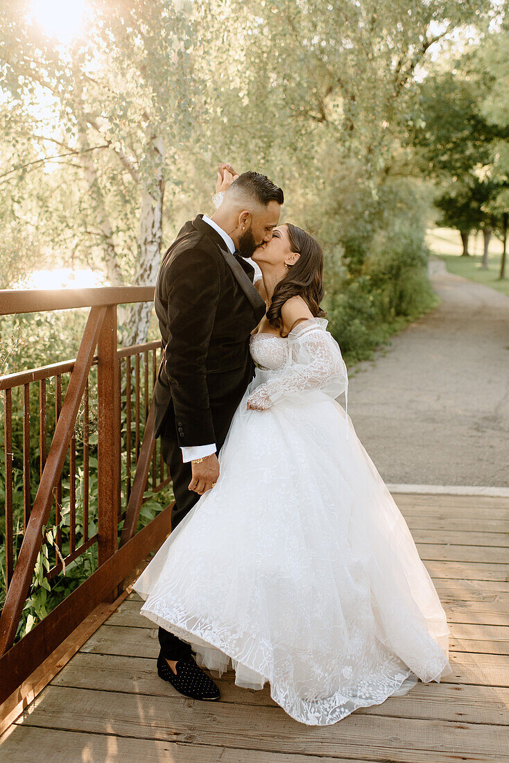 Bride and groom kissing on footbridge in park
