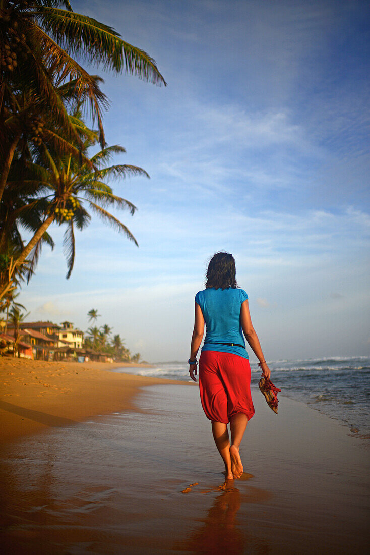 Junge Frau beim Spaziergang am Strand von Hikkaduwa bei Sonnenuntergang, Sri Lanka