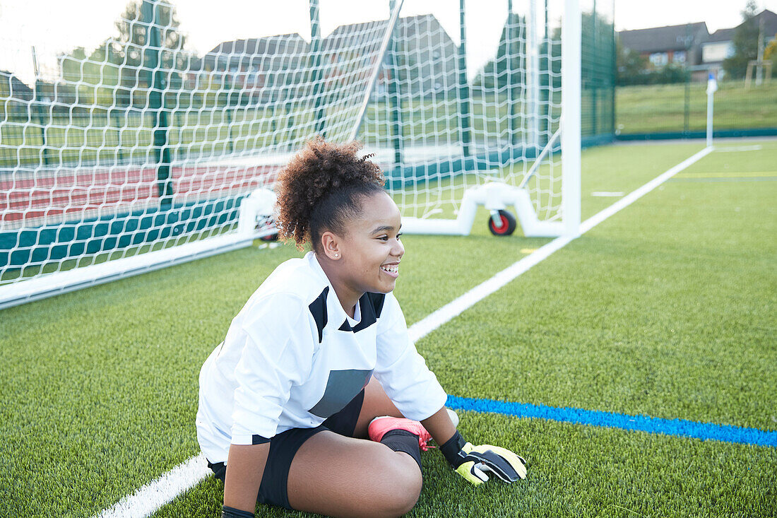 UK, Lächelnde Fußballtorfrau (12-13) sitzt in der Nähe des Tores