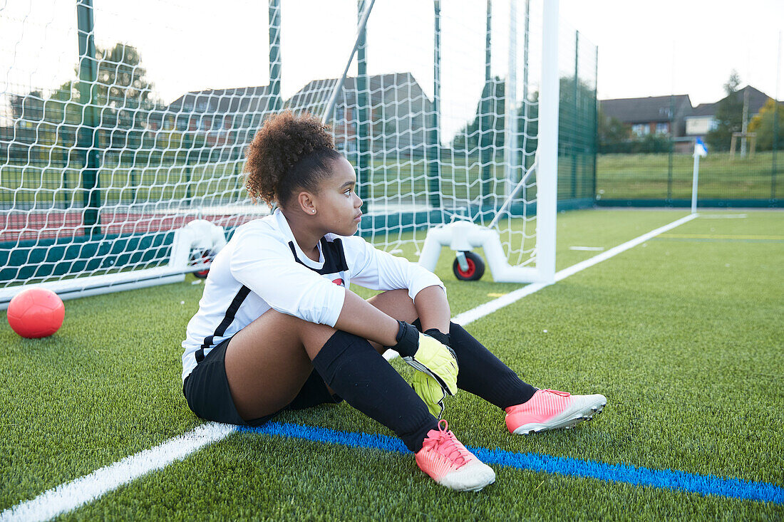 UK, Tired female soccer goalie (12-13) sitting at goal