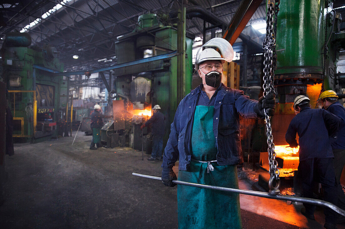 Operative prepares to hook steel billet out of furnace. Team in background using counterblow hammer