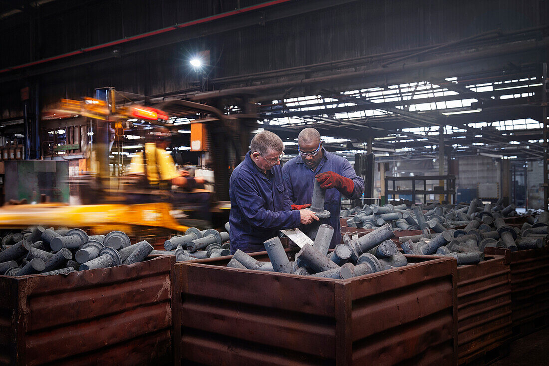 Checking dimensions on crank shafts in warehouse area as fork lift truck unloads a new steel container of product in background