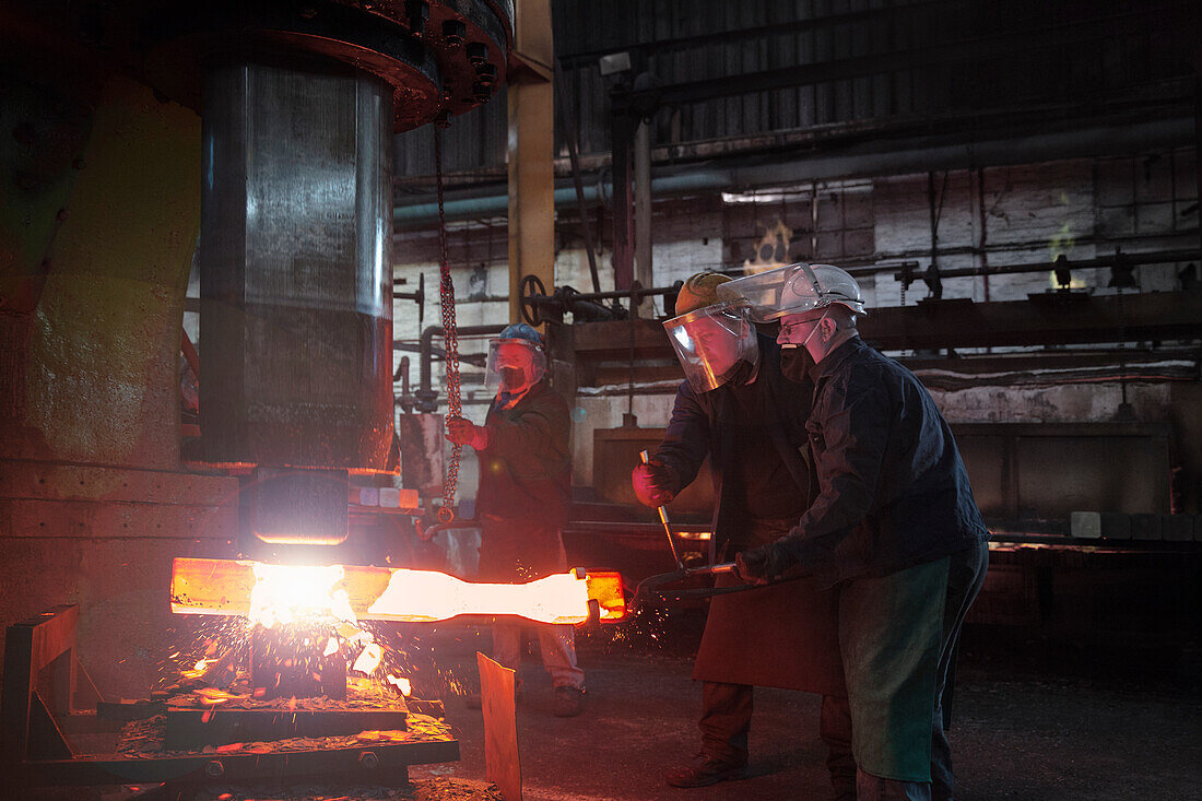 Forge workers pre form red hot steel billet into flight bar (mining component) on hammer