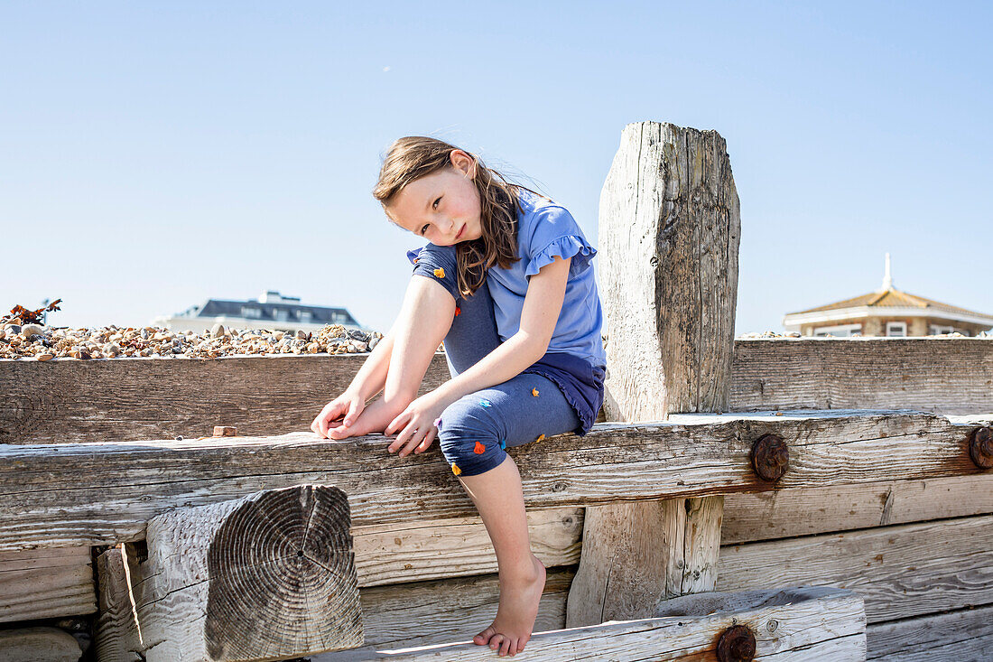 Porträt eines Mädchens (4-5), das auf einer Holzstruktur am Strand sitzt