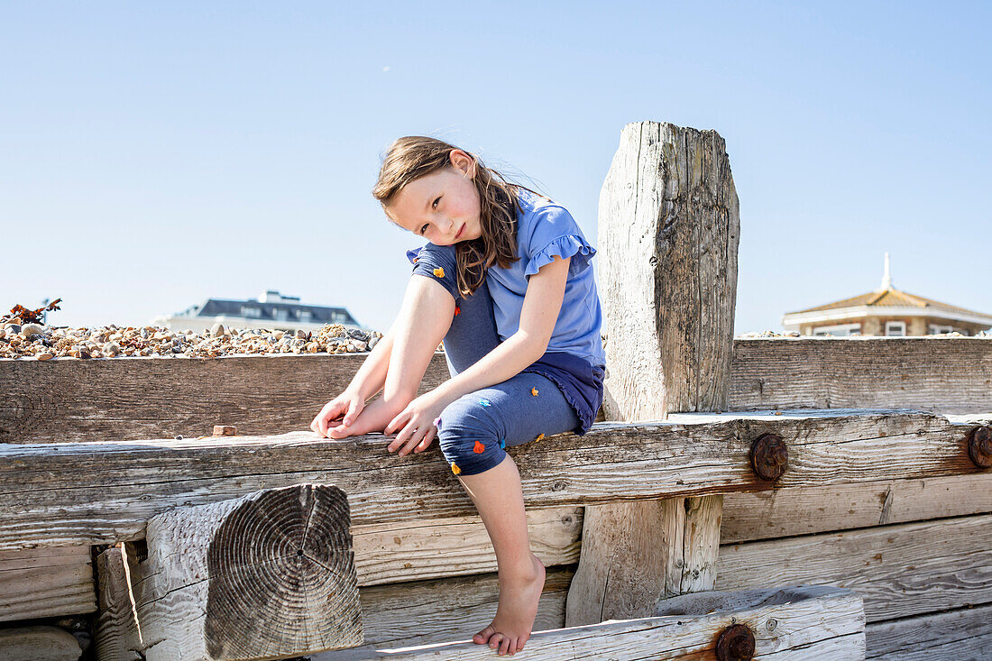 Portrait of girl (4-5) sitting on wooden structure on beach