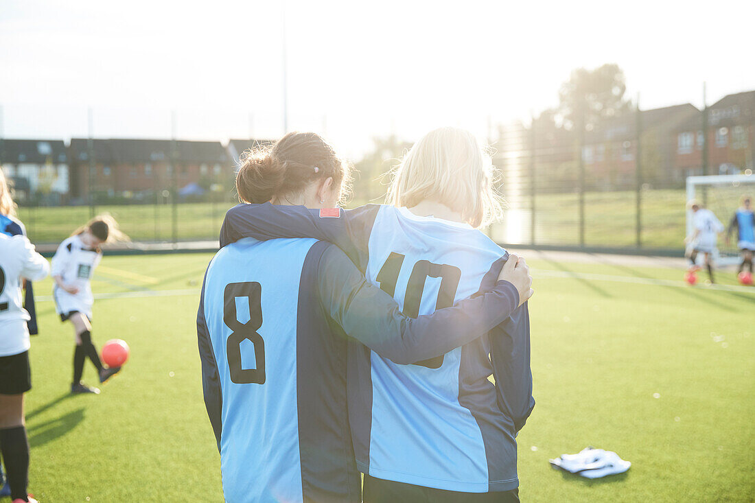 UK, Rückansicht von weiblichen Fußballspielern (10-11, 12-13), die sich auf einem Feld umarmen