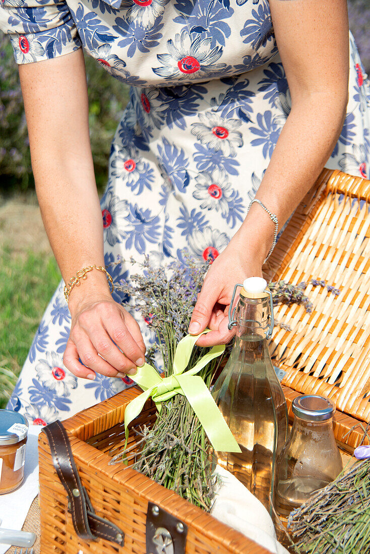 Nahaufnahme einer Frau, die einen Picknickkorb in einem Lavendelfeld arrangiert