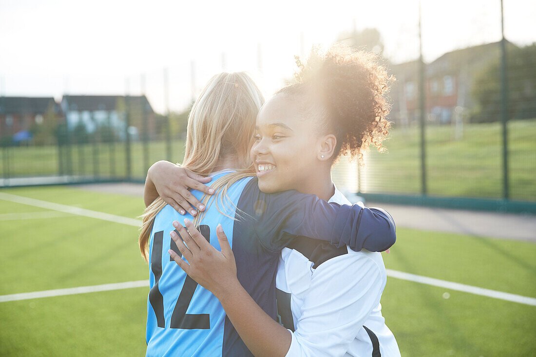 UK, Smiling female soccer team members (12-13) embracing in field
