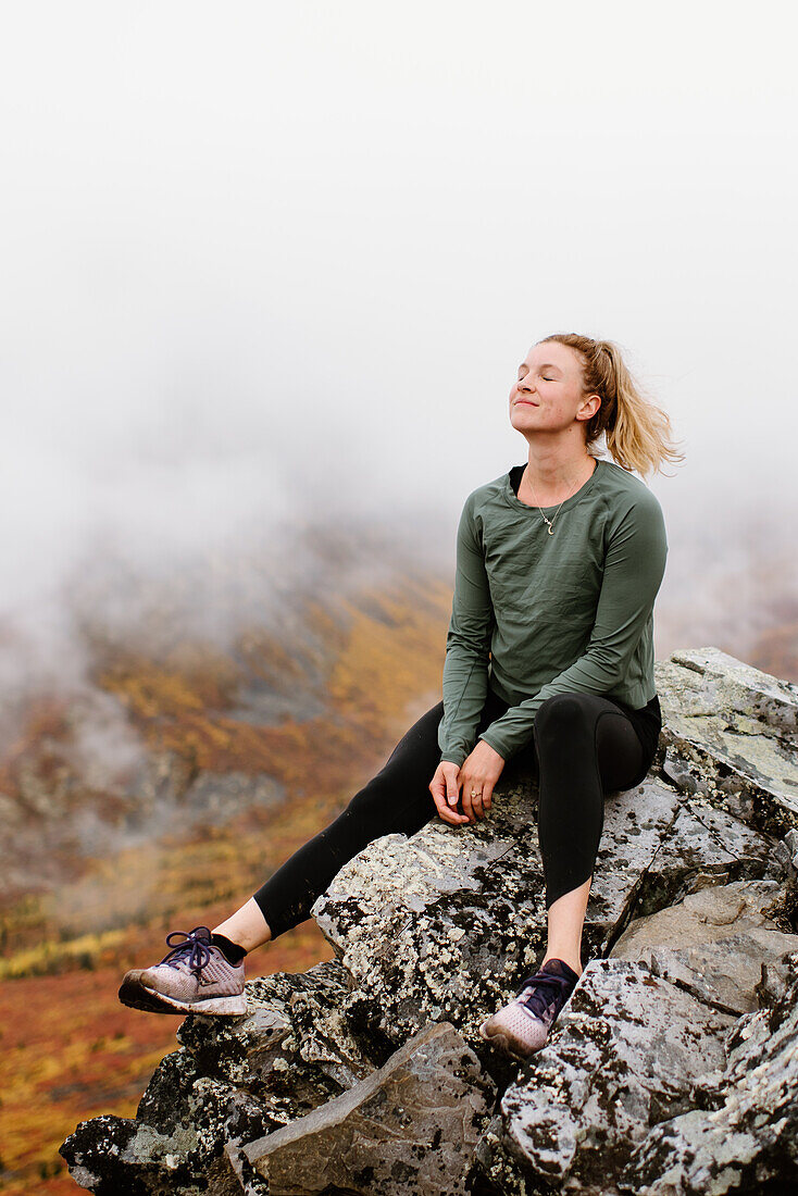 Canada, Yukon, Whitehorse, Smiling woman sitting on rock in foggy landscape