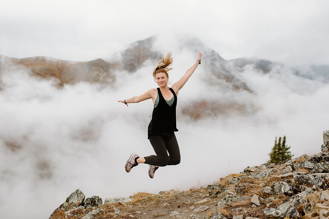 Canada, Whitehorse, Woman jumping fog covered mountain landscape