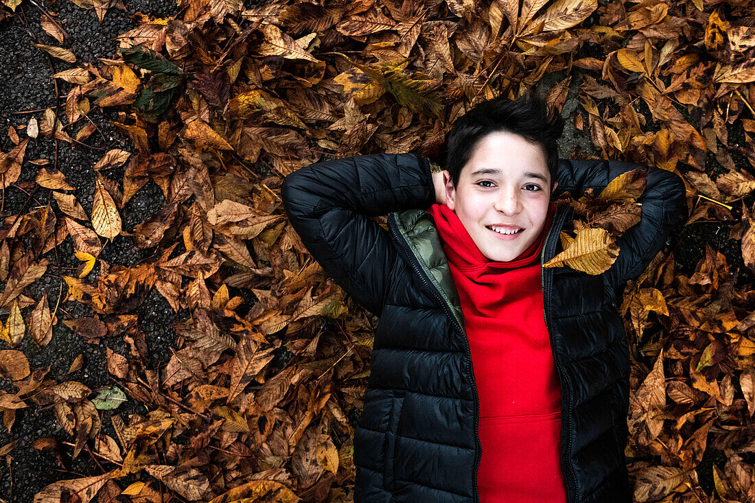 Boy lying in heap of autumn leaves
