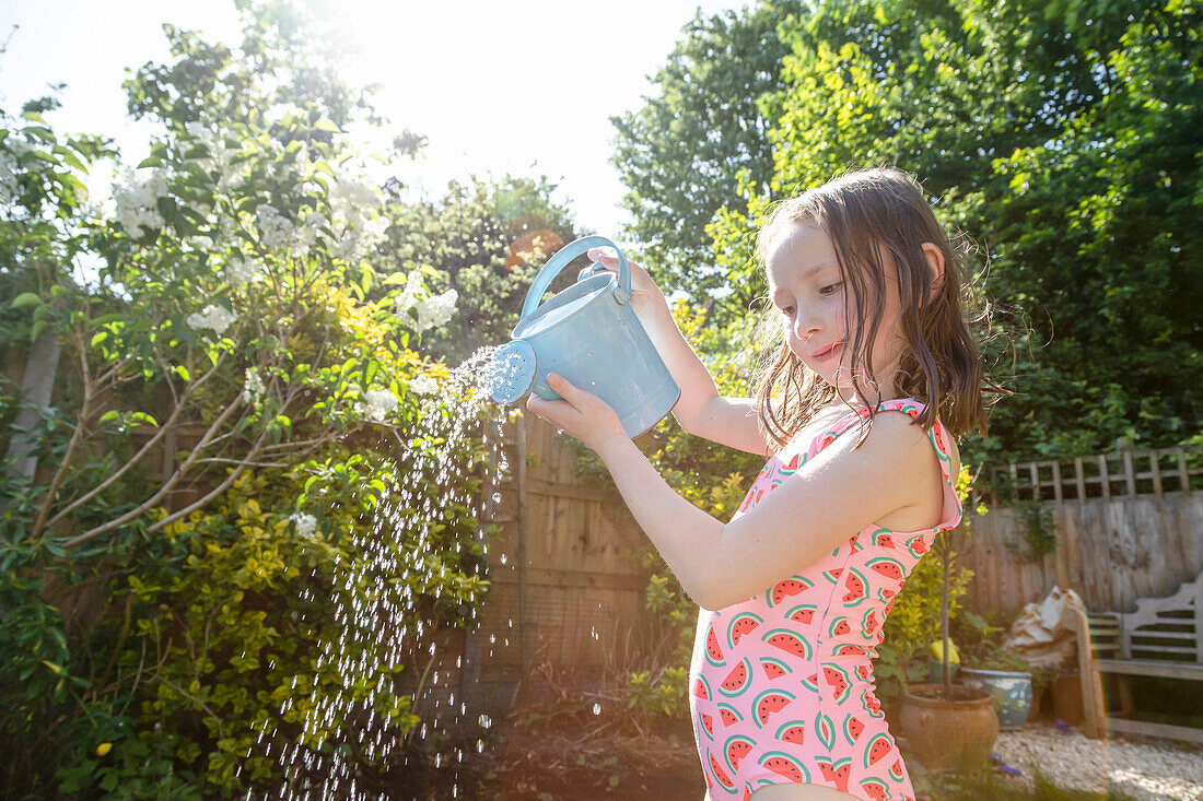 Girl (4-5) in swimsuit pouring water from watering can in garden