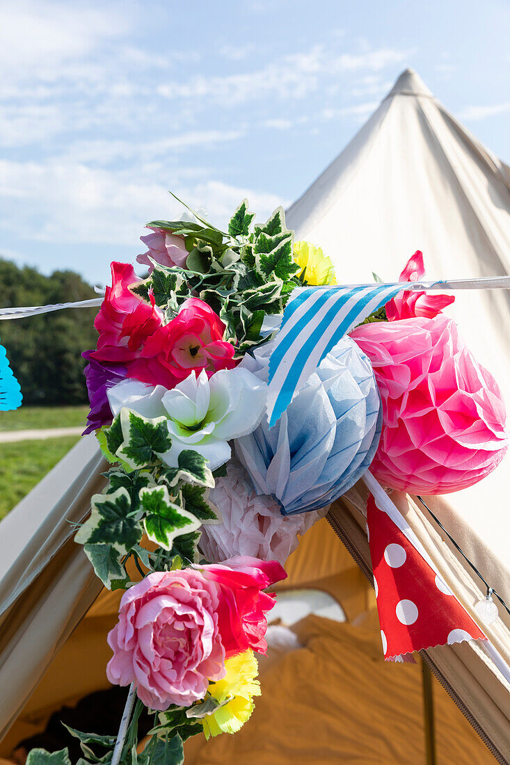 Nahaufnahme von Blumen und Papierdekorationen, die vor einem Zelt hängen