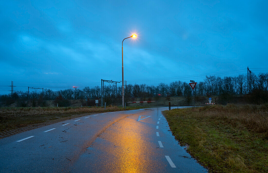 Country road with railroad crossing at dusk in rain