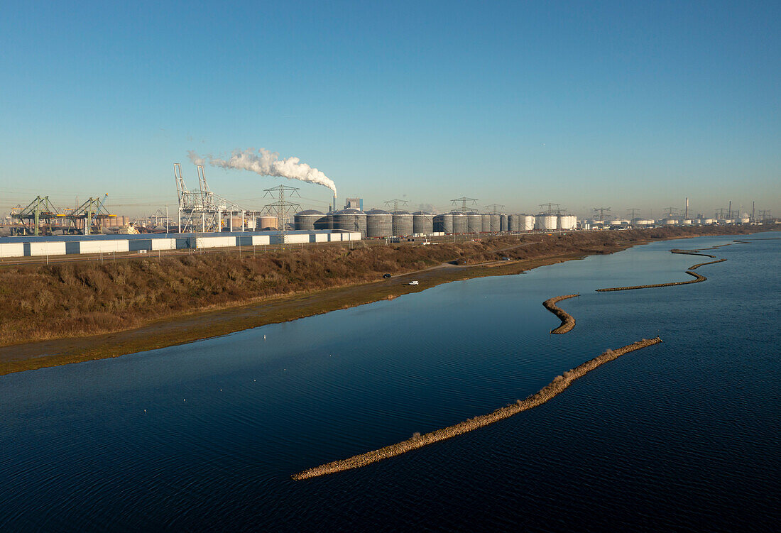 Niederlande, Oostvoorne, Fluss mit Öllagertanks und Hafenkränen