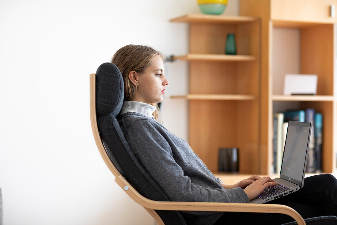 Profile of young woman using laptop at home