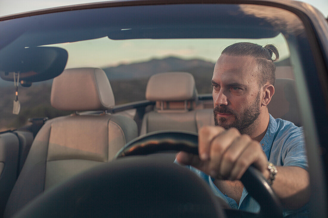 Man driving convertible car in landscape at sunset