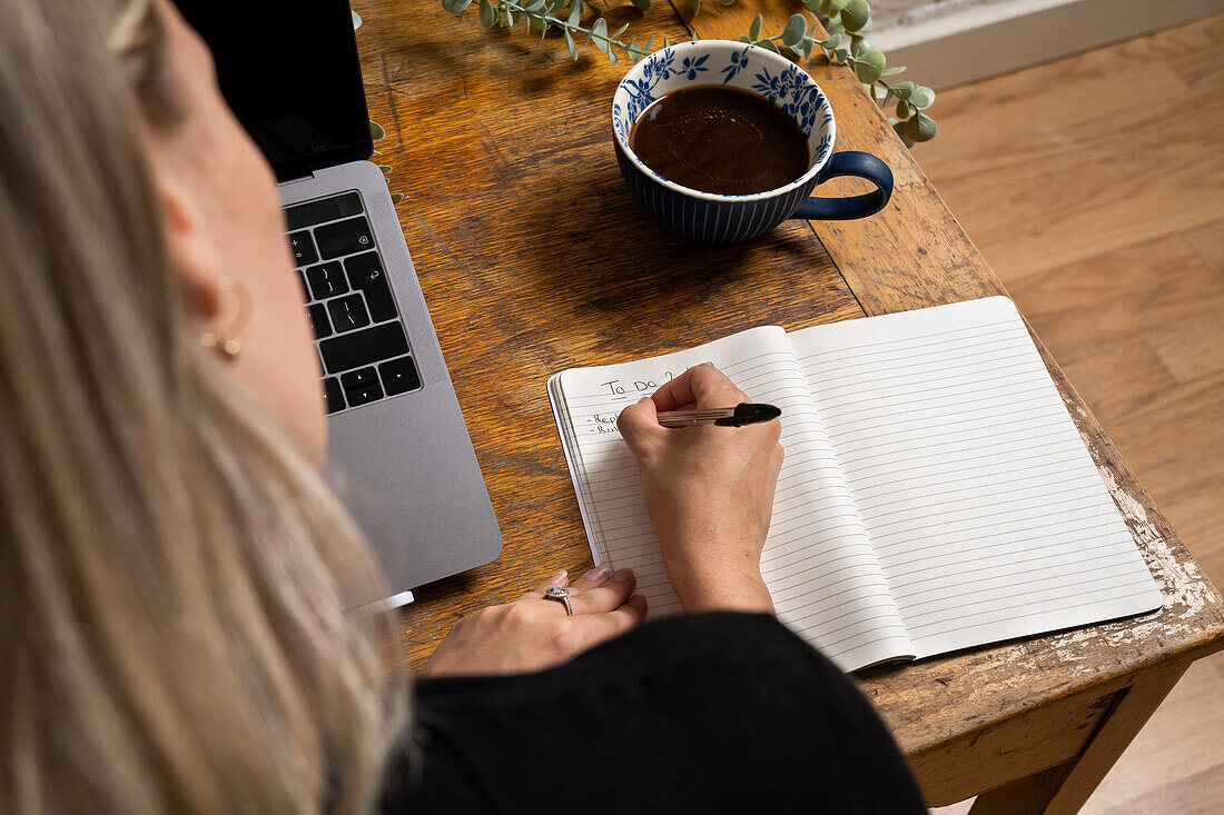 Close-up of woman writing to do list in notepad