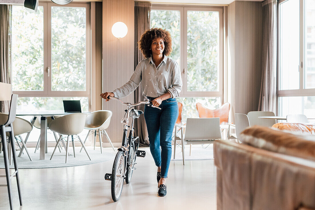 Italy, Smiling businesswoman with bicycle in creative studio