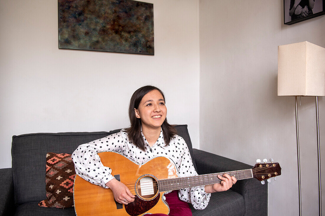 Smiling woman playing acoustic guitar in living room