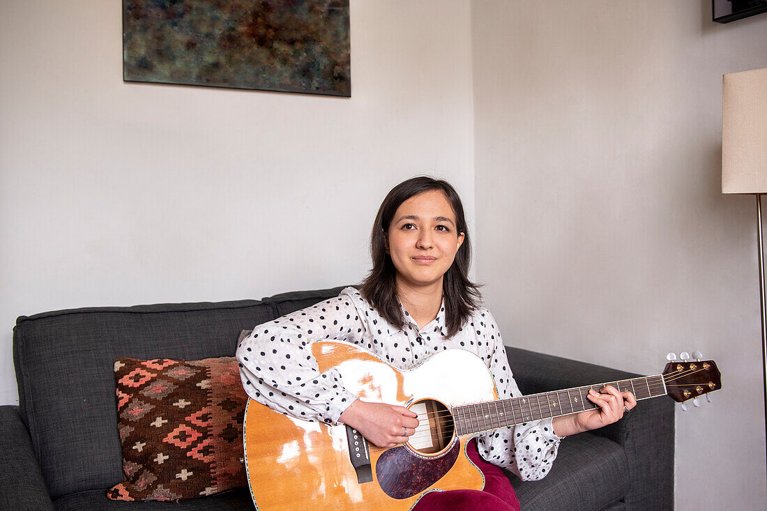 Smiling woman playing acoustic guitar in living room