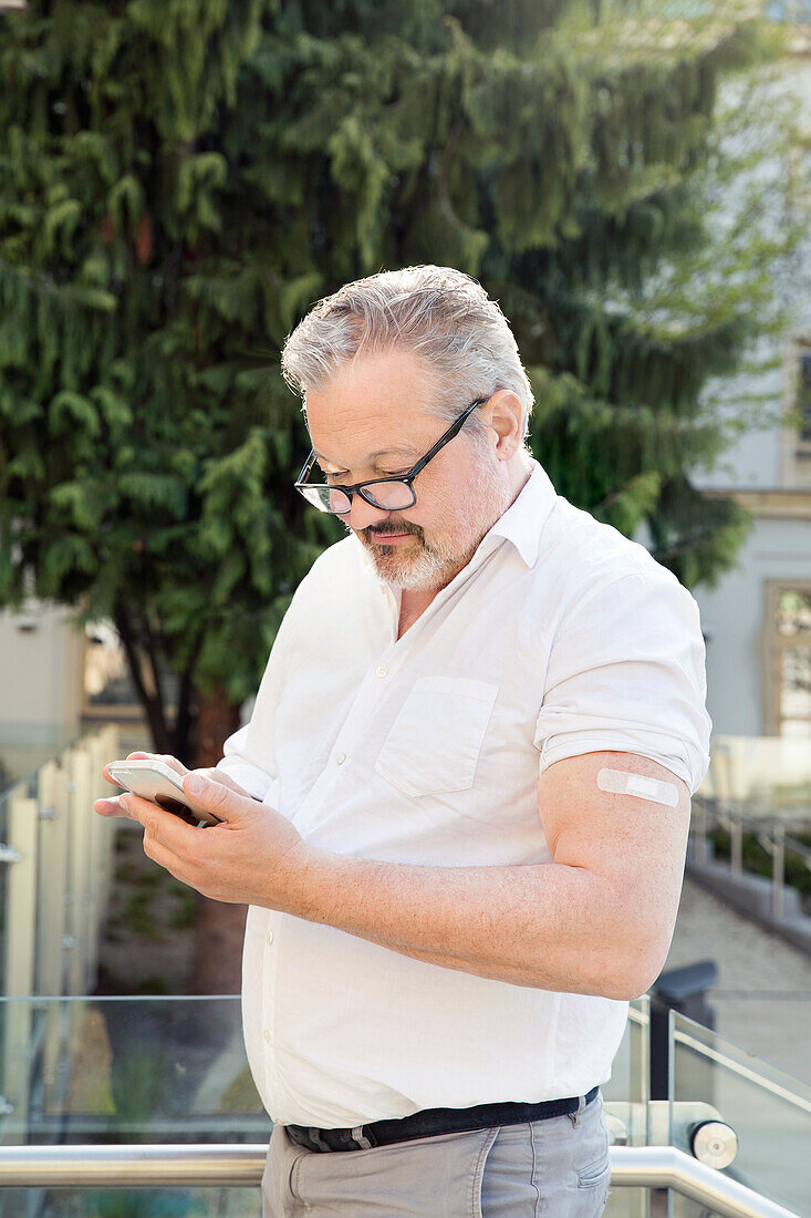 Österreich, Wien, Mann mit Klebeverband am Arm benutzt Smartphone im Freien
