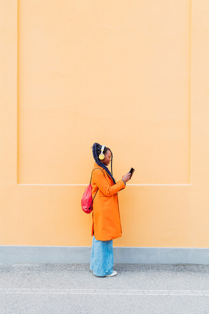 Italy, Milan, Woman with headphones and smart phone against orange wall