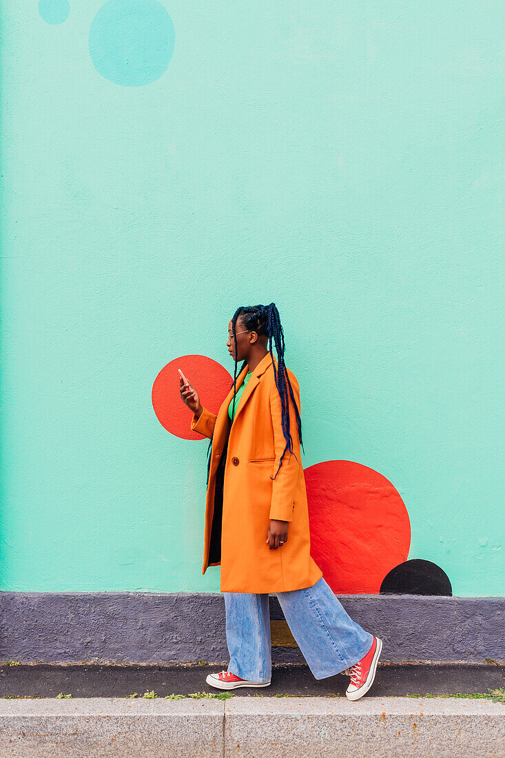 Italy, Milan, Woman with braids using smart phone against green wall