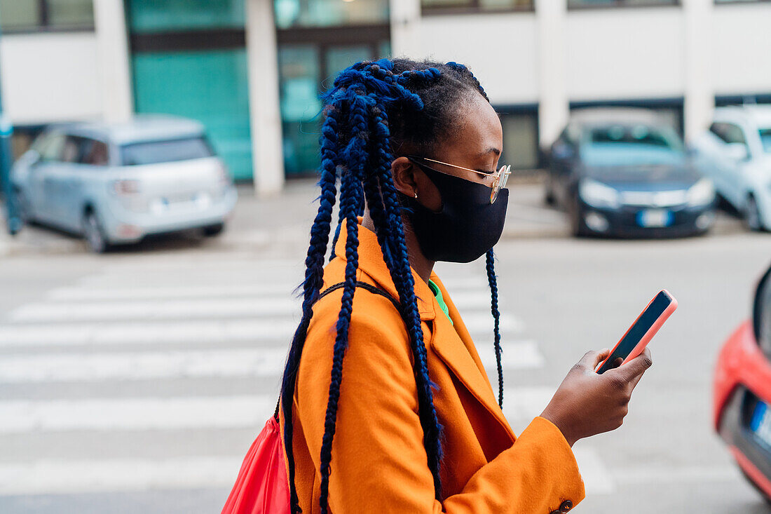 Italy, Milan, Fashionable woman with face mask holding smart phone on street