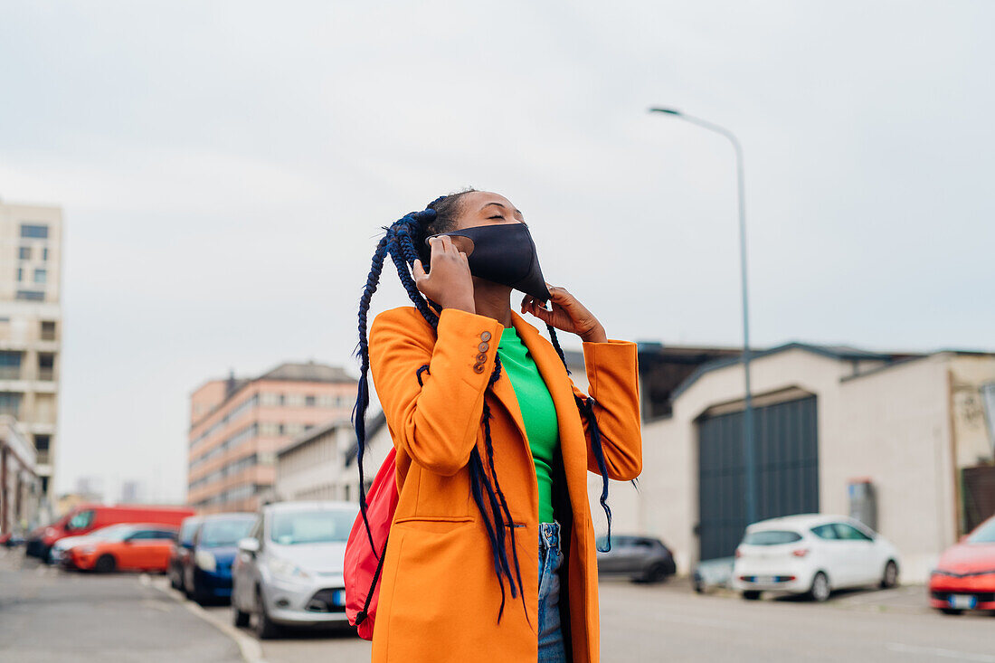 Italien, Mailand, Modische Frau nimmt Gesichtsmaske auf der Straße ab