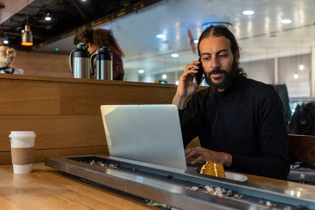 Großbritannien, London, Mann mit Laptop und Smartphone im Flughafencafé