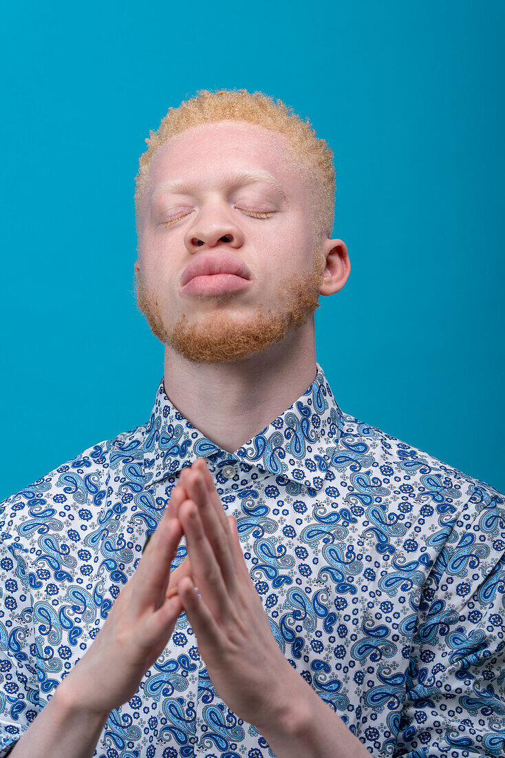 Studio portrait of albino man in blue patterned shirt with eyes closed