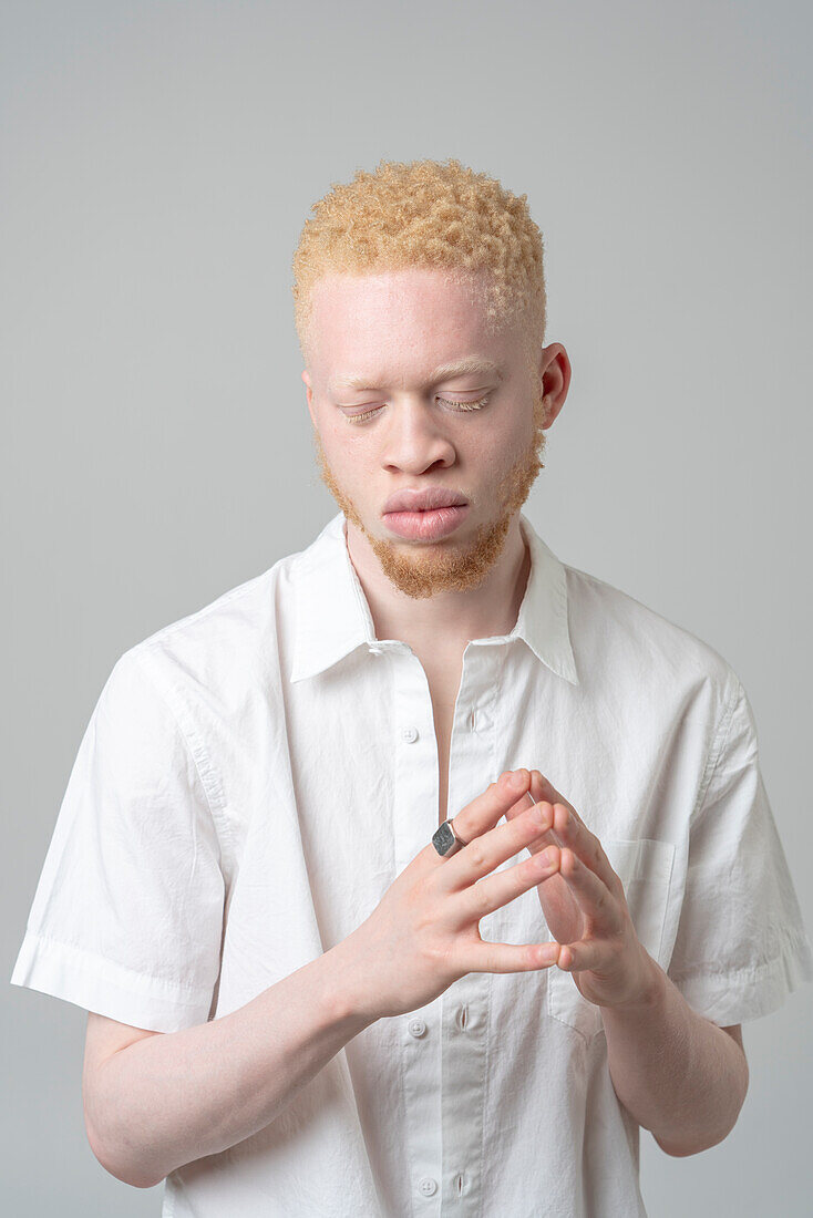 Studio portrait of albino man in white shirt with eyes closed