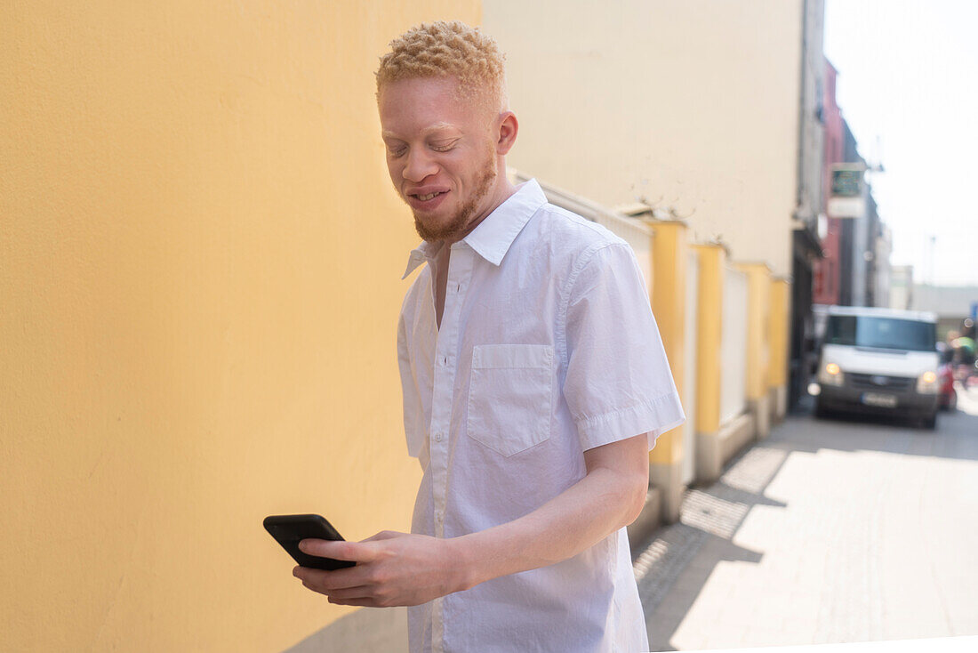 Germany, Cologne, Albino man in white shirt holding smart phone