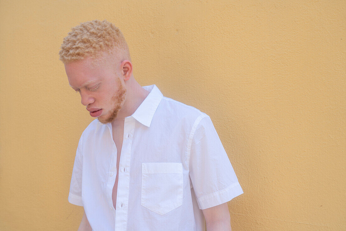 Germany, Cologne, Albino man in white shirt against yellow wall