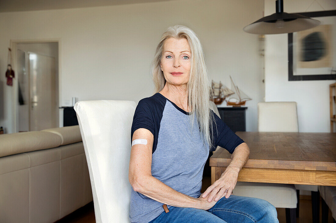 Austria, Vienna, Senior woman with adhesive bandage on arm sitting at table