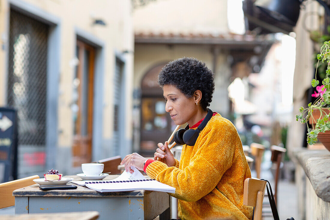 Italien, Toskana, Pistoia, Frau, die in einem Café im Freien sitzt und in Notizen blättert
