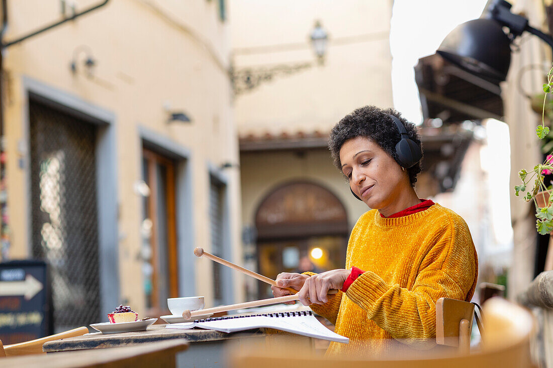 Italy, Tuscany, Pistoia, Woman practicing with drumsticks in outdoor cafe