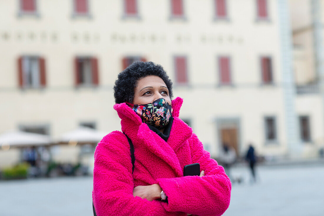 Italien, Toskana, Pistoia, Frau mit Gesichtsmaske und rosa Mantel geht durch die Stadt