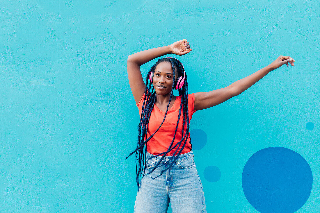 Italy, Milan, Young woman with headphones dancing in front of blue wall