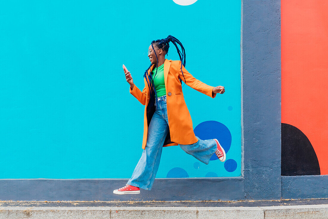 Italien, Mailand, Frau mit Zöpfen springt gegen blaue Wand