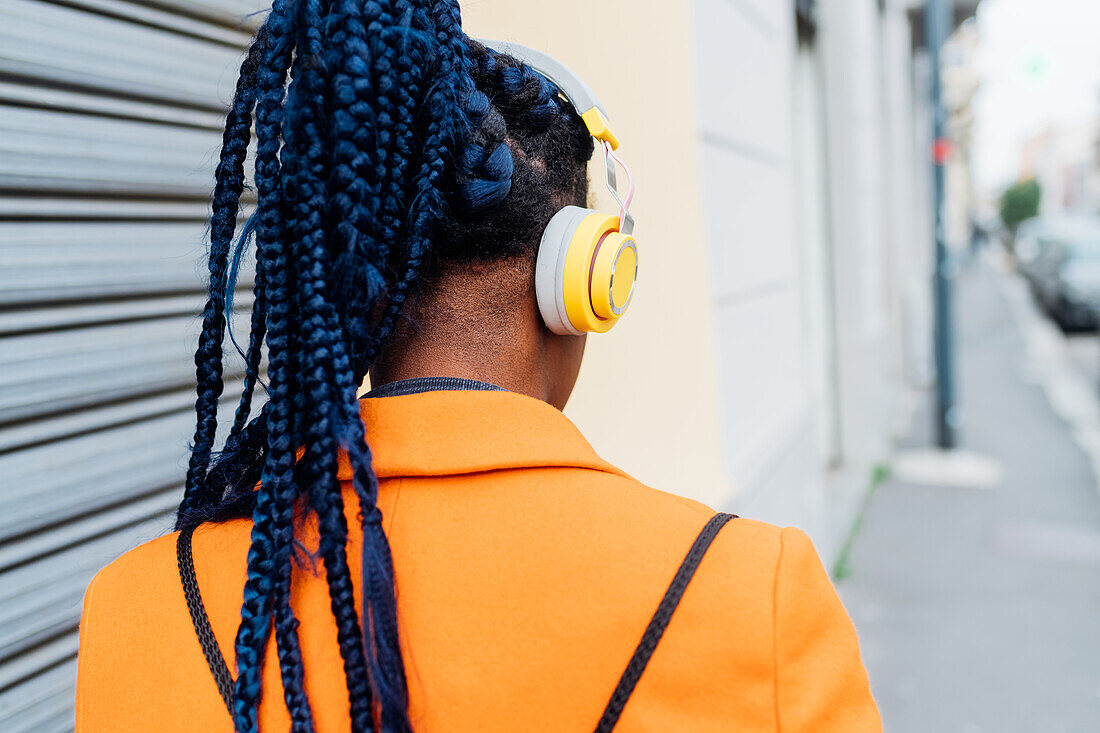 Italy, Milan, Rear view of woman with braids and headphones in city