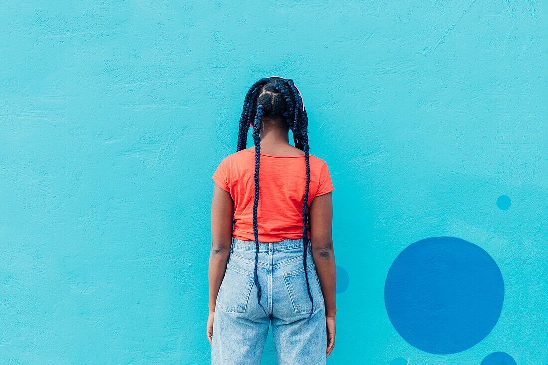 Italy, Milan, Rear view of woman with braids in front of blue wall