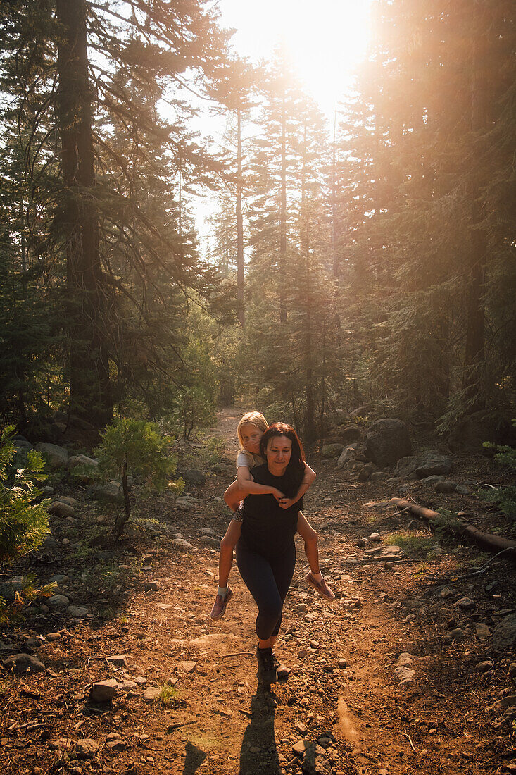 Woman giving daughter (6-7) piggyback ride while hiking