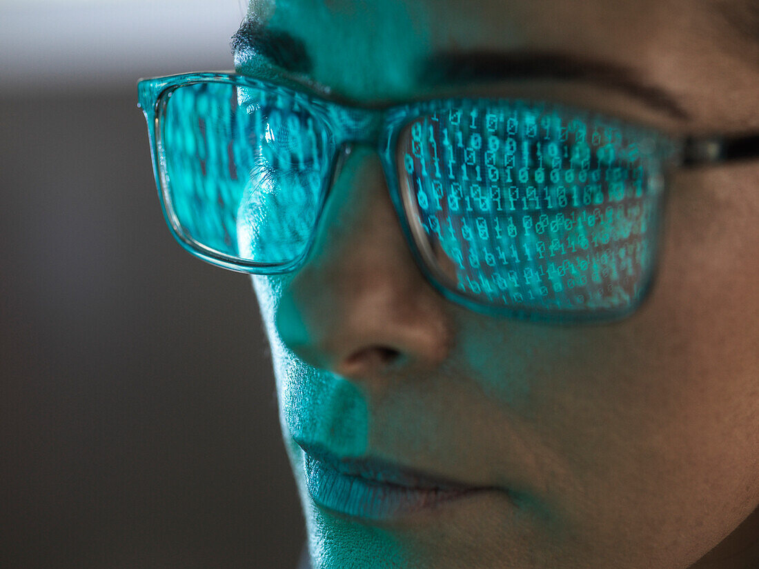 Nahaufnahme eines Programmierers mit Binärcode, der sich in der Brille spiegelt